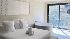 Hotellihuone, jossa on suuri sänky, pyöreä kylpyamme ja parveke, jolta on näkymä rakennuksiin.
