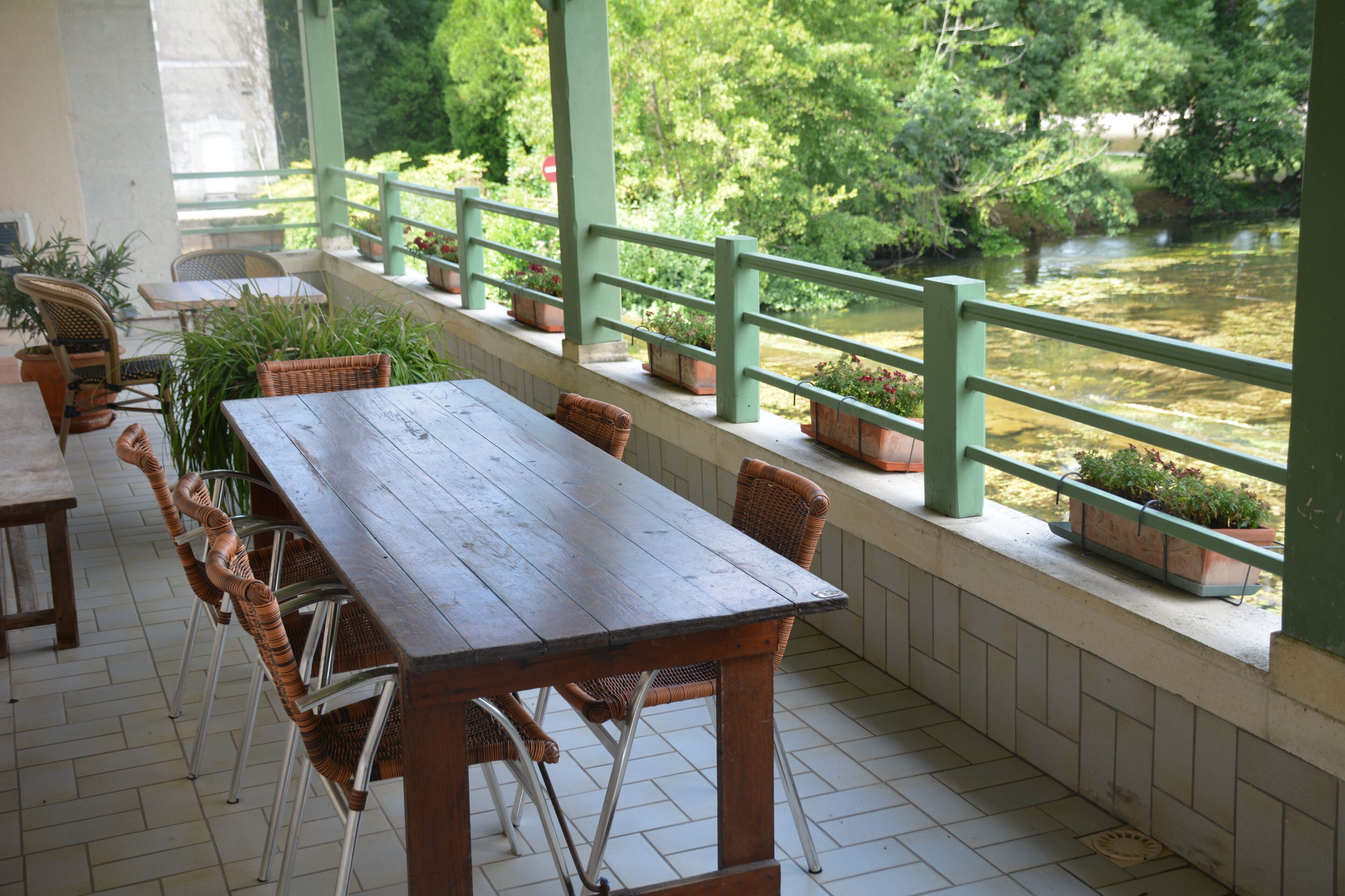 Un espace extérieur abrité, avec une table en bois et des chaises en osier, donnant sur une rivière.