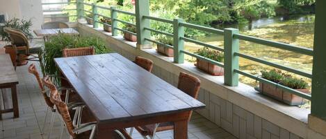 Un espace extérieur abrité, avec une table en bois et des chaises en osier, donnant sur une rivière.