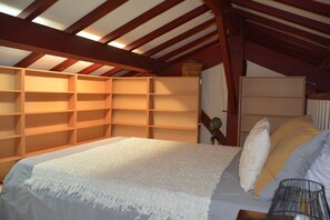 A bedroom with a sloped ceiling, wooden built-in shelves, a bed with white bedding, and a bedside lamp.