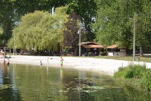 A lakeside area with a sandy beach, a small pavilion, and a row of bicycles.