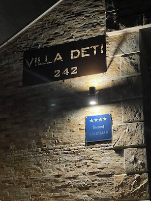 Eine Steinsäule mit einem Schild, auf dem 'VILLA DETI 242' steht, sowie ein blaues Schild mit Sternen und dem Wort 'APARTMAN'.