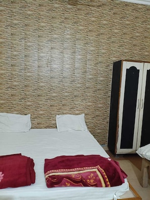 A room with a stone-textured wall, a bed with white bedding, and a wardrobe with black and white doors. - Hotel Chaitanya Inn  (Varanasi)