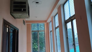 A hallway with large windows, a ceiling fan, and an air conditioning unit. - Hotel Chaitanya Inn  (Varanasi)