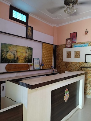 Un mostrador de recepción con un emblema decorativo, un cuadro enmarcado de Buda, un letrero en la pared y un ventilador de techo.