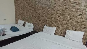 A hotel room with two beds, a stone-textured wall, and a white bedspread. - Hotel Chaitanya Inn  (Varanasi)