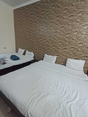 Habitación de hotel con dos camas, pared de textura pétrea y una colcha blanca.