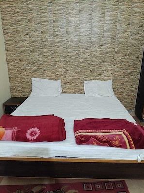 A bed with white linens, two pillows, and two red blankets with floral patterns. - Hotel Chaitanya Inn  (Varanasi)