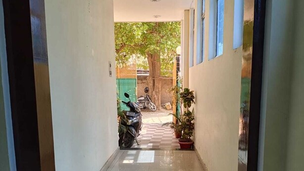 A corridor with tiled flooring, a tree outside, and a parked motorcycle. - Hotel Chaitanya Inn  (Varanasi)