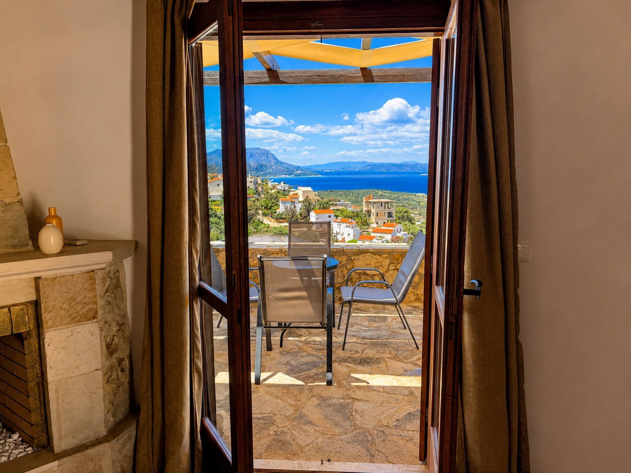Een open deur die leidt naar een balkon met uitzicht op een kustlandschap, een tafel en een stoel.