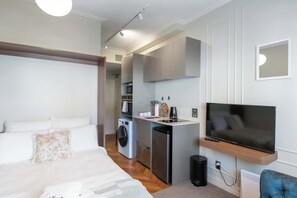 A compact hotel room with a bed, a small kitchenette, a washing machine, and a TV. - Te Aro City Stay - Modern Studio for Two (Wellington)