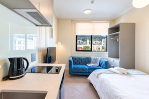 A modern hotel room with a kitchenette, a sofa, a bed, and a large window offering a city view. - Te Aro Studio | City Views + Laundry (Wellington)