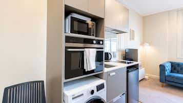 A compact kitchenette with a microwave, oven, and built-in washing machine.