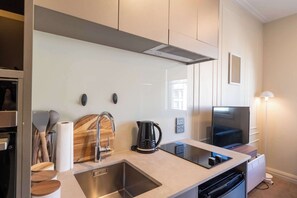 A modern kitchen with a stainless steel sink, wooden cutting board, kettle, and a flat-screen TV. - Te Aro City Stay - Modern Studio for Two (Wellington)