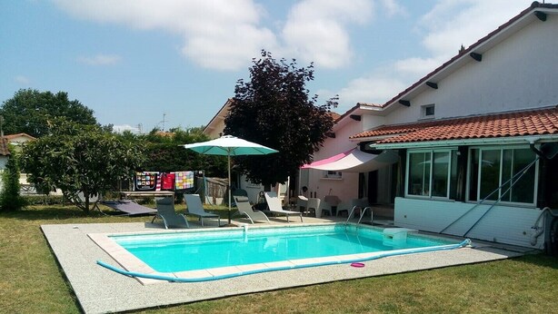 A swimming pool with lounge chairs and umbrellas, a covered patio, and a house with a tiled roof. - Three rooms at "Chez Valou & Mika" in Mont de Marsan, Landes. (Mont-de-Marsan)