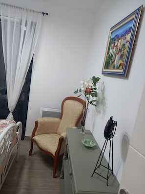 Une pièce comprenant un lit, une chaise, un radiateur, un tableau encadré et un vase avec des fleurs.
