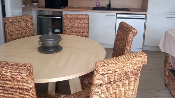 Une cuisine moderne avec des armoires blanches, une hotte noire et une table de salle à manger ronde entourée de chaises en osier.