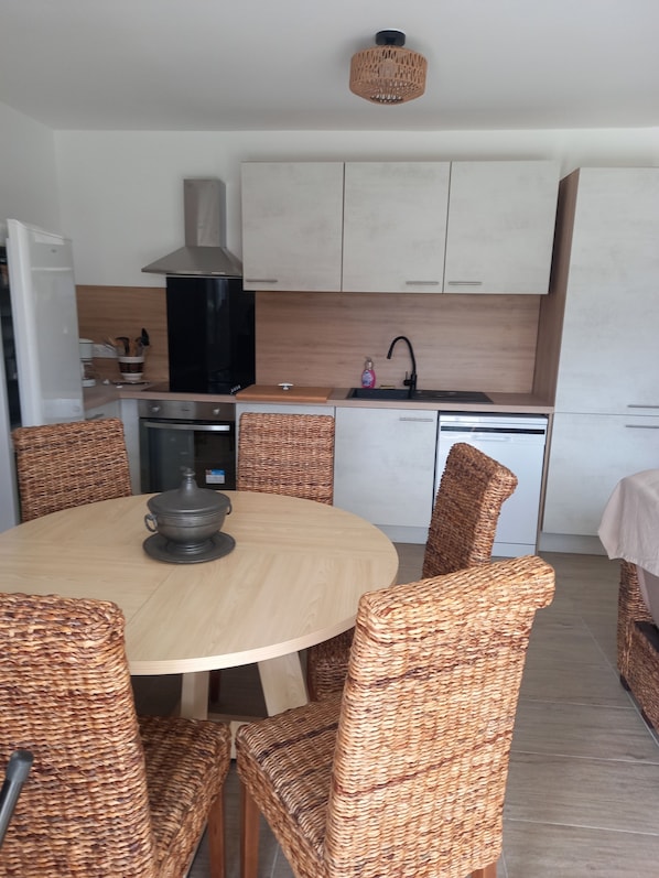Une cuisine moderne avec des armoires blanches, une hotte noire et une table de salle à manger ronde entourée de chaises en osier.