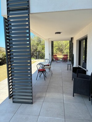 A covered patio area with outdoor furniture, including chairs and a table, and a view of the surrounding landscape. - Summer rentals by the sea in South Corsica (Propriano)