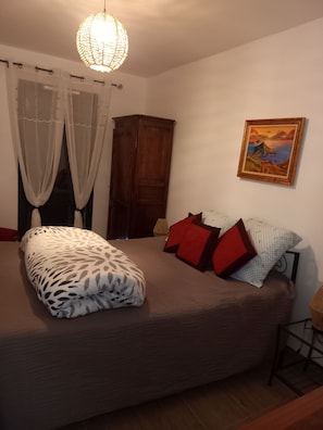 Une chambre à coucher avec un lit, une armoire en bois, un tableau au mur et un luminaire suspendu.