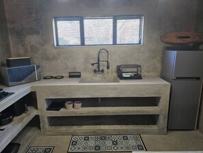 A kitchen with a built-in sink, a window above it, a microwave, a kettle, a kettle holder, a dish rack, a refrigerator, and a patterned mat on the floor. - Tranquil Bush Escape, Private House With Pool in Marloth Park (Nkomazi)