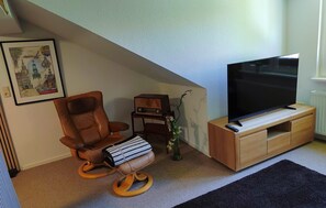 Ein Wohnzimmer mit einem braunen Ledersessel, einem Holz-TV-Möbel, einem gerahmten Bild und einem kleinen Tisch mit einer Vase.