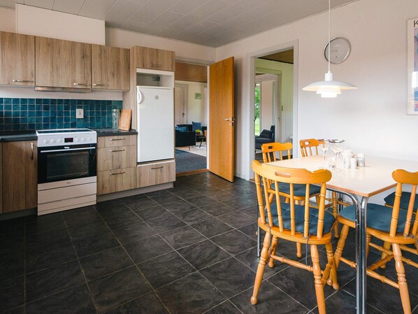 Una cocina moderna con suelo de baldosas oscuras, armarios de madera y una zona de comedor con mesa y sillas.