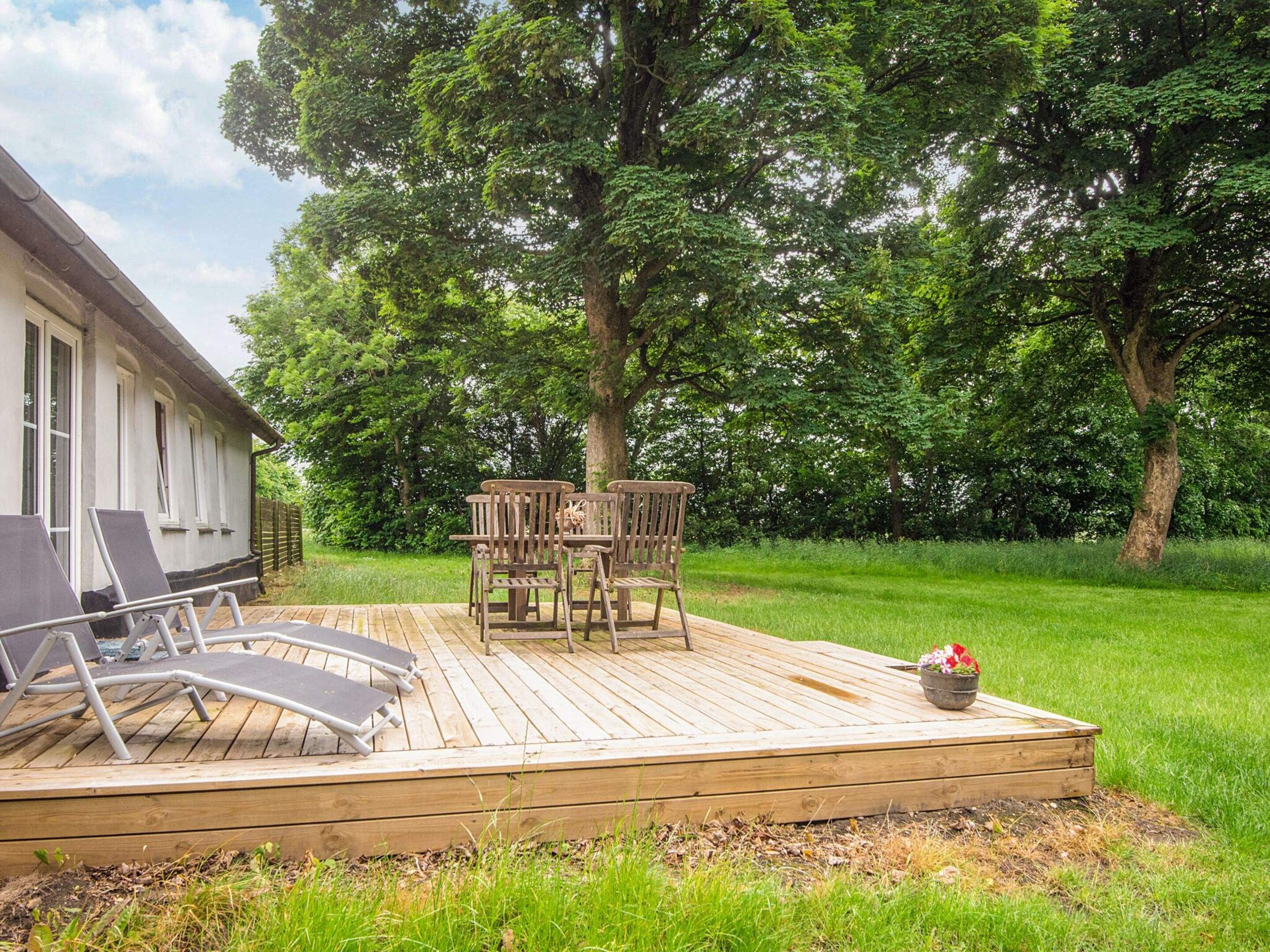 A wooden deck with outdoor furniture, including chairs and a table, surrounded by lush greenery and trees.