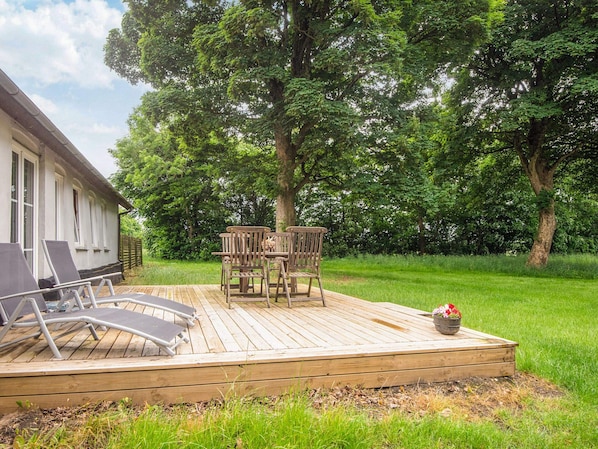 Una terraza de madera con mobiliario exterior, incluyendo sillas y una mesa, rodeada de exuberante vegetación y árboles.