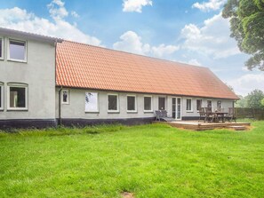 A single-story building with a tiled roof, a grassy yard, and a patio with outdoor furniture.