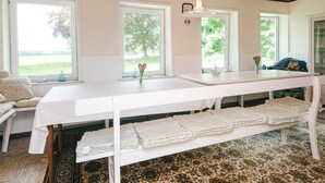 Ein Zimmer mit einem weißen Tisch, zwei Fenstern, einer Bank mit gefalteten Handtüchern und einem gemusterten Teppich.