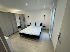 A bedroom with a bed, two bedside tables, a window, and a door. - Very quiet, renovated 58 m2 apartment 100m from the sea (La Seyne-sur-Mer)