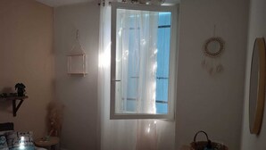Un dormitorio con cama, cortinas en una ventana, una mesita de noche, un estante en la pared y un adorno mural.