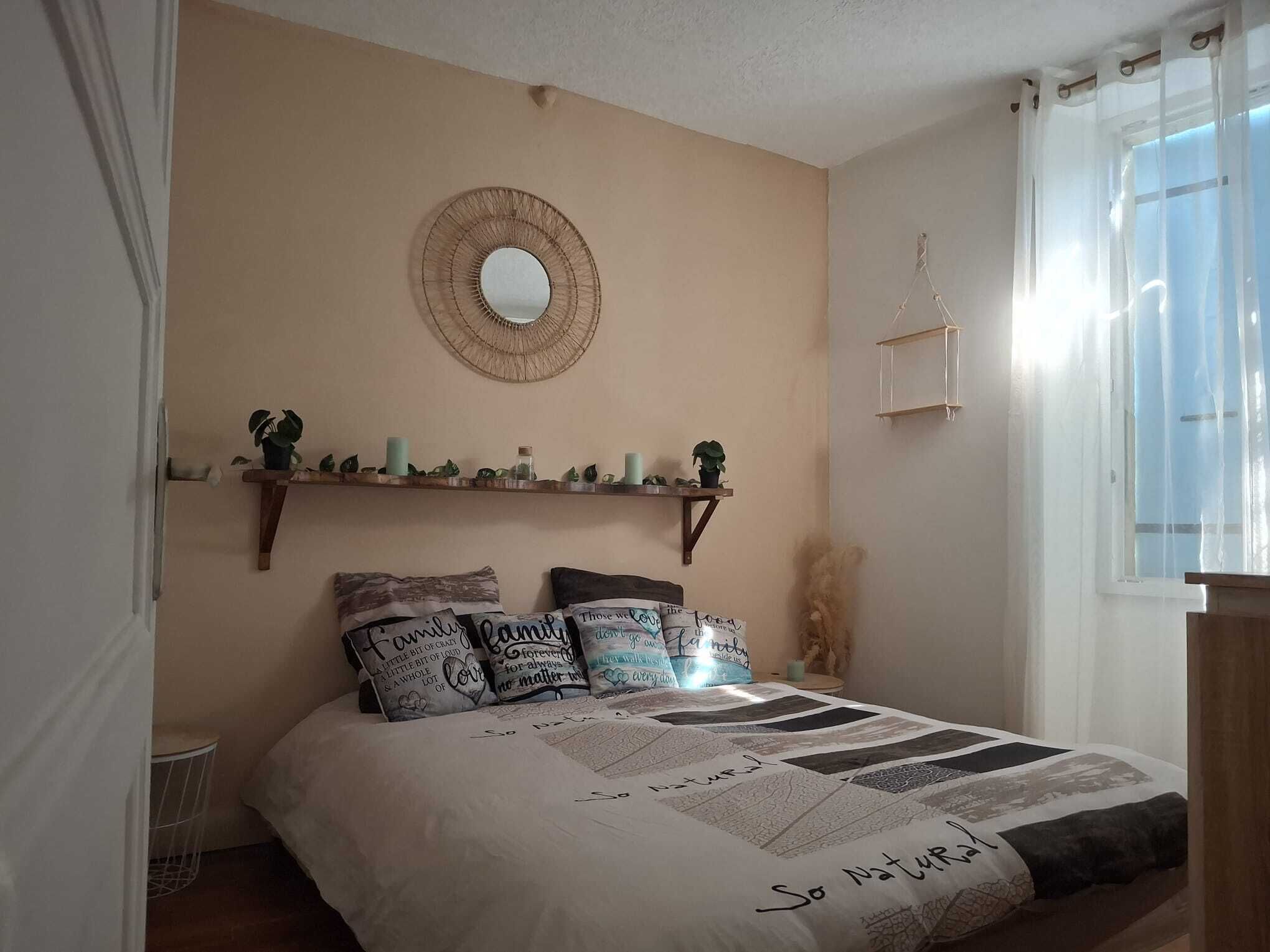 A bedroom with a bed, a round mirror, shelves with decorative items, and a window with curtains.
