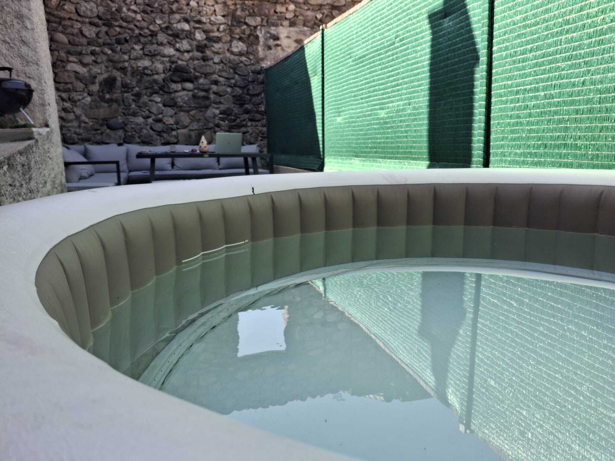A circular pool with a stone wall and a green netted area in the background.. Cosy house 4 persons