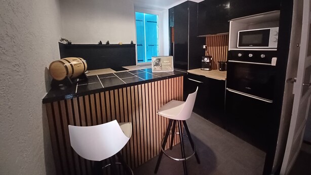 Una cocina moderna con encimera negra, taburetes blancos, una isla de madera y un microondas empotrado.