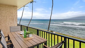 A wooden table with chairs, a bottle, and a plant on a balcony overlooking the ocean. - 1BR ocean-view condo in West Maui with pool, hot tub, kitchen-Papakea F210 (Lahaina)