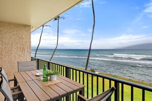 Ein Holztisch mit Stühlen, einer Flasche und einer Pflanze auf einem Balkon mit Blick auf den Ozean.
