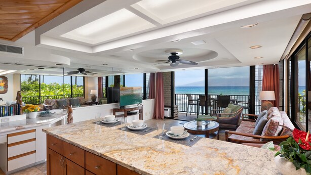 A spacious kitchen with a large island, a dining area with a view of the ocean, and a balcony with outdoor seating. - 1BR ocean-view condo in West Maui with pool, hot tub, kitchen-Papakea F210 (Lahaina)