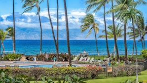 A pool area with lounge chairs, palm trees, and a view of the ocean. - 1BR ocean-view condo in West Maui with pool, hot tub, kitchen-Papakea F210 (Lahaina)