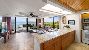 A modern kitchen with a large island, a dining area with a view, and a balcony with a view. - 1BR ocean-view condo in West Maui with pool, hot tub, kitchen-Papakea F210 (Lahaina)