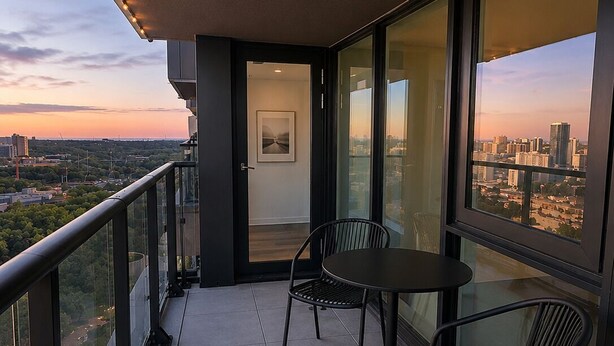 Een balkon met een tafel en stoelen, een deur die naar een binnenruimte leidt, en een stadszicht.