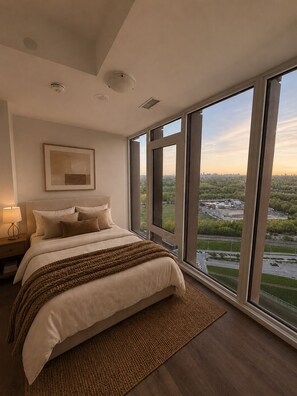 Ein modernes Schlafzimmer mit einem großen Bett, einem Nachttisch, einem gerahmten Bild und Blick auf eine Stadtlandschaft durch große Fenster.