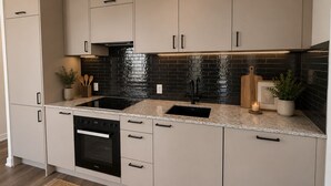 Een moderne keuken met een zwart betegelde spatwand, roestvrijstalen apparatuur en lichtkleurige kastjes.