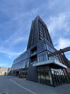 Ein modernes Hochhaus mit Glasfassade, einem markanten Eingang mit Glastür und blauem Himmel im Hintergrund.