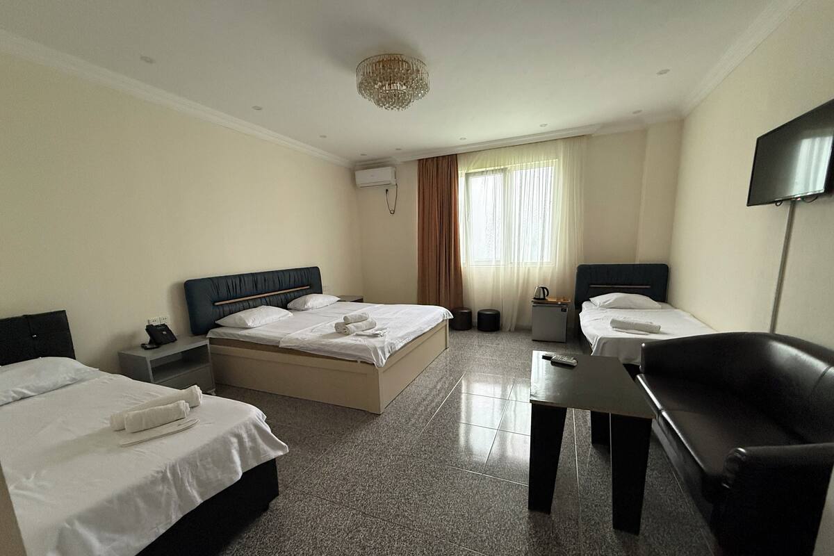 A hotel room with two beds, a desk, a chair, a TV, and a chandelier.
