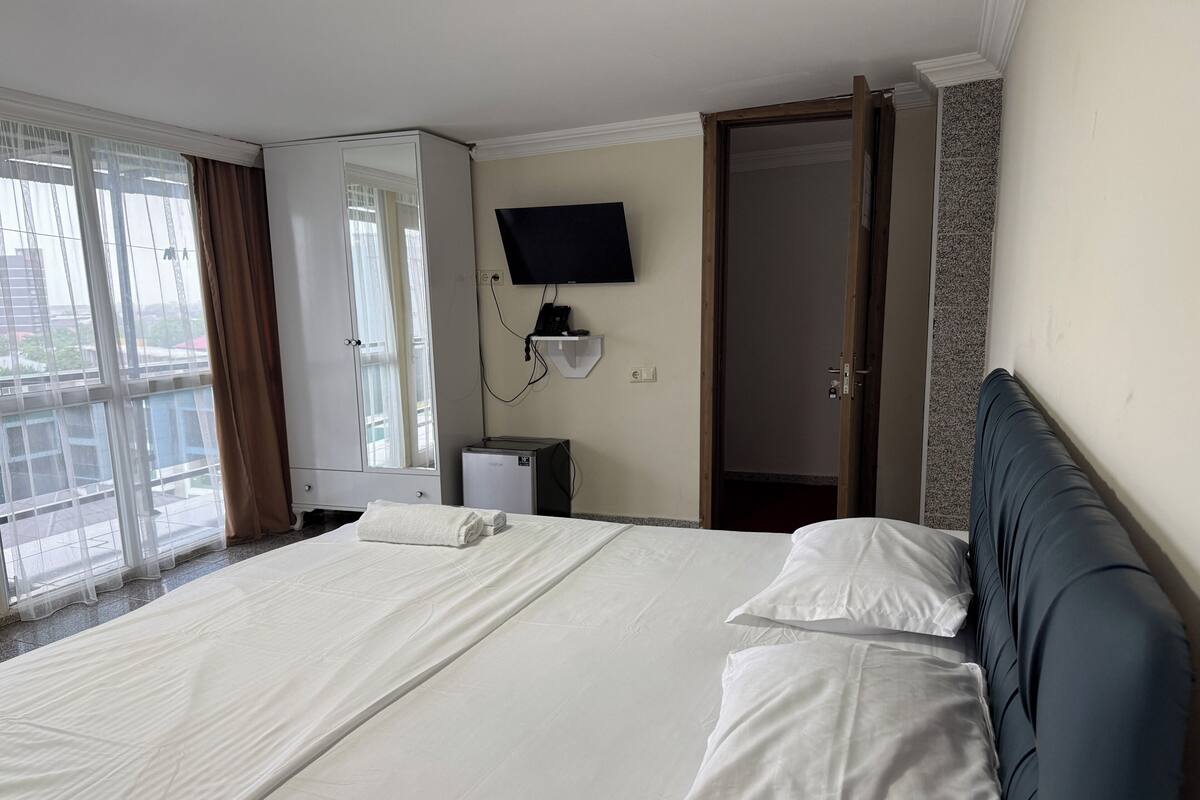 A hotel room with a large bed, a television mounted on the wall, and a sliding door leading to a balcony.