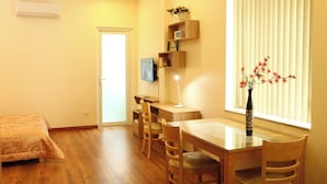 A room with a bed, a desk, a chair, a table, a vase with flowers, and a window with blinds. - 1-bedroom apartment windows, balcony, full kitchen, Bathtub in Ho Chi Minh City (Ho Chi Minh City)
