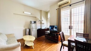 A compact living space with a sofa, a small round table, a TV, a kitchenette, and a window with curtains. - 1-bedroom apartment windows, balcony, full kitchen, Bathtub in Ho Chi Minh City (Ho Chi Minh City)