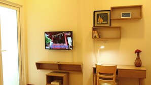 A room with a TV mounted on the wall, a desk with a chair, wooden shelves, and a vase with flowers. - 1-bedroom apartment windows, balcony, full kitchen, Bathtub in Ho Chi Minh City (Ho Chi Minh City)